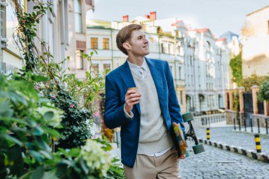 Gülümseyen yakışıklı iş adamı. Takım elbiseli. Elinde kahve ve uzun tahta bir sokak var.