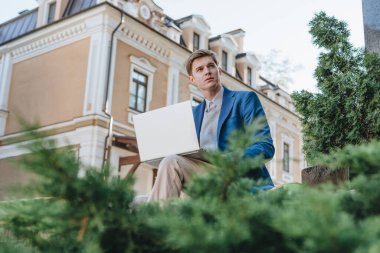 Serbest çalışan, takım elbiseli genç bir işadamı dışarıda, sörf tahtasında oturuyor..