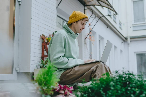 stock image Freelancer young man working on laptop sitting on the stairs on the street. Selective focus.