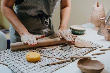 Genç bayan çömlekçi atölyede kil yuvarlıyor. Kadın ellerine yakın çekim. Seçici odak.
