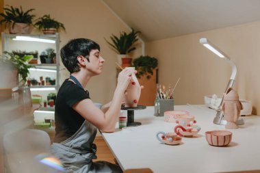 Sanat stüdyosunda çömlekçi olarak vazo boyayan genç kadın. Seçici odak.