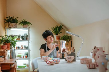 Genç bir kadın atölyesinde el yapımı bir vazo boyuyor. Seçici odak.