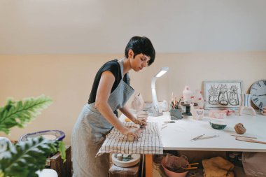 Genç bayan çömlekçi atölyesinde kil yuvarlıyor. Seçici odak.