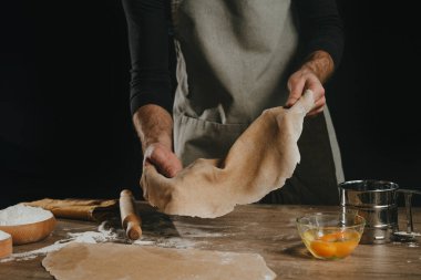Karanlık bir arka plana karşı elinde ince bir hamur tutan tanınmaz bir adam. Erkek eli yakın çekim, ev yapımı erişte hazırlıyor. Seçici odak.
