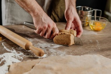Ahşap bir arka planda bıçakla hamuru kesen tanınmaz bir adam. Erkek eli yakın çekim, ev yapımı erişte hazırlıyor. Seçici odak.