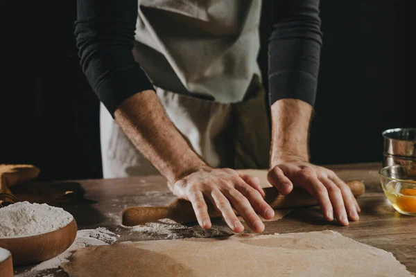 暗い壁を背景に木製の背景にローリングピンで生地を展開認識できない男 男性の手を閉じる自家製麺を修復します 選択的焦点 — ストック写真
