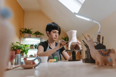 Atölyede çalışan kadın seramikçi masada bir vazo yapıyor. Seçici odak.