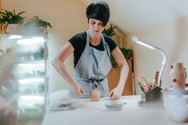 Dişi esnaf çömlekçi atölyede özel bir aletle kil kesiyor. Seçici odak.