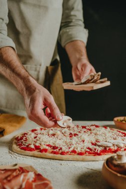 Şefin hamurun üzerine mantar koyarak pizza hazırladığı yakın plan. Seçici odak.