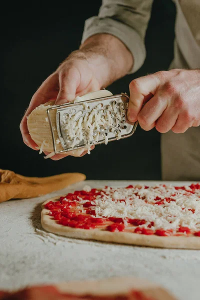 Großaufnahme Des Küchenchefs Bei Der Zubereitung Von Pizzabreibekäse Mit Einer lizenzfreie Stockfotos