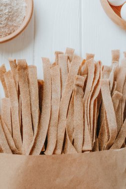 El yapımı çiğ makarna kağıdı, beyaz masanın üzerinde el yapımı kağıt bir torbada tam tahıllı undan yapılmış ve mesaj için boş bir alan var. Üst manzara, düz uzanma.