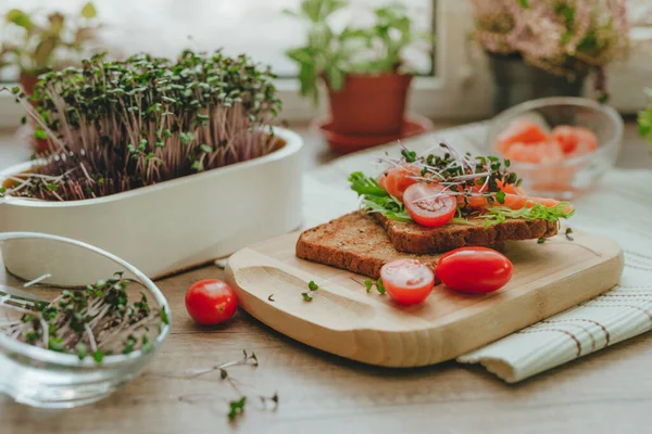 stock image Sandwich with salmon fish, microgreens of radish and tomato on wooden background. Idea of homegrown vitamin food. Selective focus.