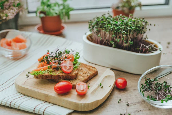 stock image Sandwich with salmon fish, microgreens of radish and tomato on wooden background. Idea of homegrown vitamin food. Selective focus.