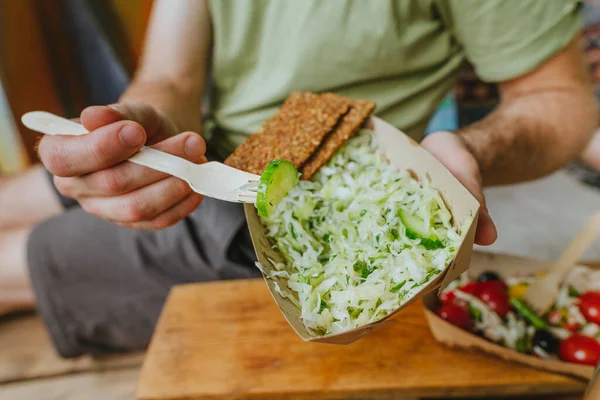 Close-up of young man having healthy lunch. Vegetable salad in a craft paper lunch box container.