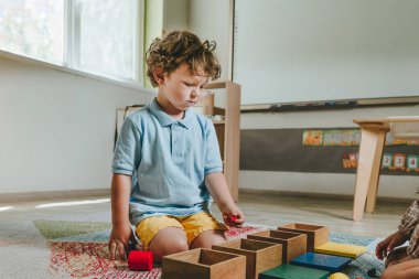Çocuk bir anaokulunda yerde tahta oyuncakları sınıflandırıyor. Seçici odak.