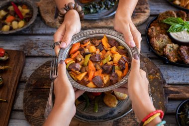 Meat stew with vegetables at the hands of two women. Orman kebabi . Cooked foods in the copper plate or pot. 