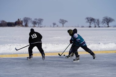 Oshkosh, Wisconsin ABD - 4 Şubat 2023: Buz tutmuş bir göl üzerinde birlikte hokey oynayan bir grup erkek arkadaş.
