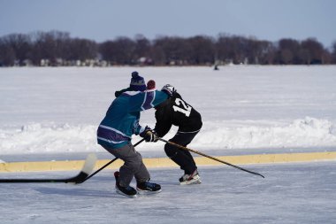 Oshkosh, Wisconsin ABD - 4 Şubat 2023: Buz tutmuş bir göl üzerinde birlikte hokey oynayan bir grup erkek arkadaş.