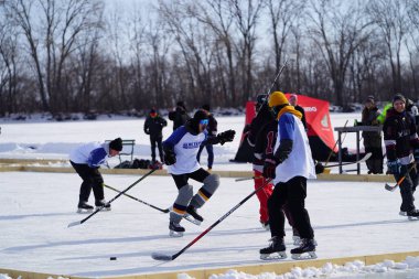 Oshkosh, Wisconsin ABD - 4 Şubat 2023: Buz tutmuş bir göl üzerinde birlikte hokey oynayan bir grup erkek arkadaş.