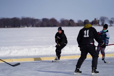 Oshkosh, Wisconsin ABD - 4 Şubat 2023: Buz tutmuş bir göl üzerinde birlikte hokey oynayan bir grup erkek arkadaş.