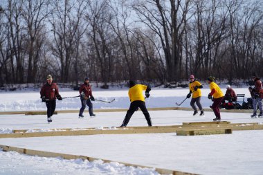 Oshkosh, Wisconsin ABD - 4 Şubat 2023: Buz tutmuş bir göl üzerinde birlikte hokey oynayan bir grup erkek arkadaş.