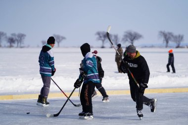 Oshkosh, Wisconsin ABD - 4 Şubat 2023: Buz tutmuş bir göl üzerinde birlikte hokey oynayan bir grup erkek arkadaş.