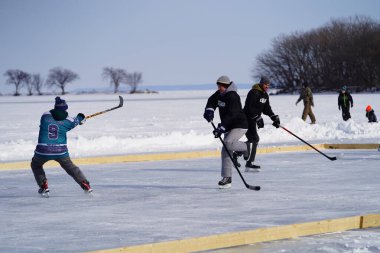 Oshkosh, Wisconsin ABD - 4 Şubat 2023: Buz tutmuş bir göl üzerinde birlikte hokey oynayan bir grup erkek arkadaş.