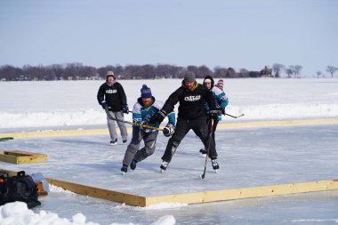 Oshkosh, Wisconsin ABD - 4 Şubat 2023: Buz tutmuş bir göl üzerinde birlikte hokey oynayan bir grup erkek arkadaş.