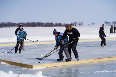 Oshkosh, Wisconsin ABD - 4 Şubat 2023: Buz tutmuş bir göl üzerinde birlikte hokey oynayan bir grup erkek arkadaş.