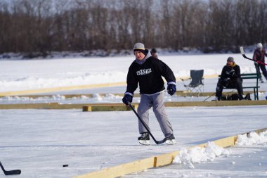 Oshkosh, Wisconsin ABD - 4 Şubat 2023: Buz tutmuş bir göl üzerinde birlikte hokey oynayan bir grup erkek arkadaş.