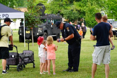 Fond du Lac, Wisconsin USA - August 1st, 2023: Local Police, sheriff and firefighter officers gathered together with community families for the National Night Out family fun event clipart