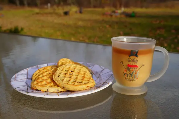 Glass Christmas coffee mug with coffee and creamer alongside a plate of chocolate chip waffles.