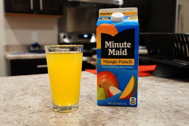 Fond du Lac, Wisconsin USA - 15 Şubat 2024: Büyük bir karton Minute Maid Mango Punch aromalı meyve suyu berrak bir bardak portakal suyunun yanında duruyor.