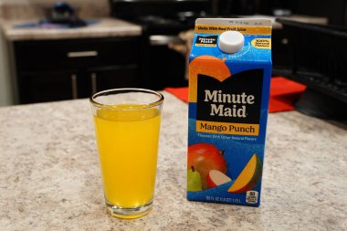 Fond du Lac, Wisconsin USA - 15 Şubat 2024: Büyük bir karton Minute Maid Mango Punch aromalı meyve suyu berrak bir bardak portakal suyunun yanında duruyor.