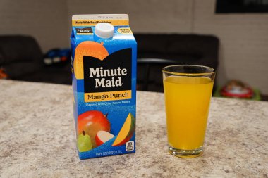Fond du Lac, Wisconsin USA - 15 Şubat 2024: Büyük bir karton Minute Maid Mango Punch aromalı meyve suyu berrak bir bardak portakal suyunun yanında duruyor.