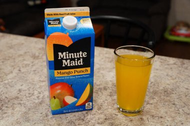 Fond du Lac, Wisconsin USA - 15 Şubat 2024: Büyük bir karton Minute Maid Mango Punch aromalı meyve suyu berrak bir bardak portakal suyunun yanında duruyor.