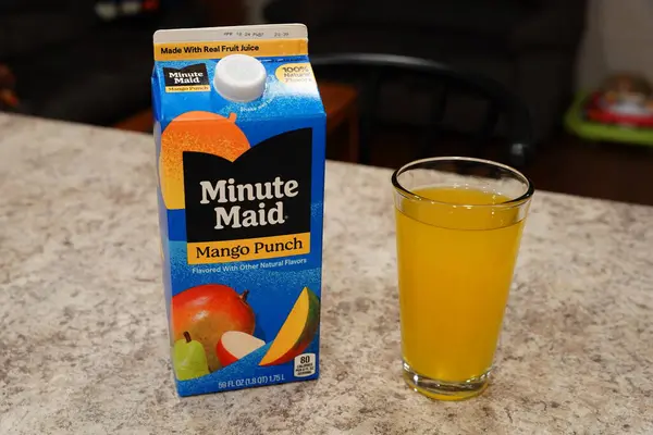 Fond du Lac, Wisconsin USA - 15 Şubat 2024: Büyük bir karton Minute Maid Mango Punch aromalı meyve suyu berrak bir bardak portakal suyunun yanında duruyor.