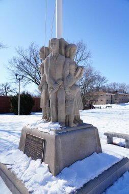 Greendale, Wisconsin / USA - February 21st, 2020: Stone Sculptures reflecting the people of the community sculpted by Alonzo Hauser in 1938 for the town center American flag Pole. Parkland Kiwanis. clipart