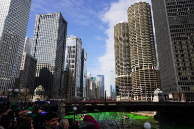 Chicago, Illinois USA - March 16th, 2024: Spectators dressed in St. Patrick colors and costumes stood and watched the Green color dyeing of the Chicago River standing in front of the Trump building clipart