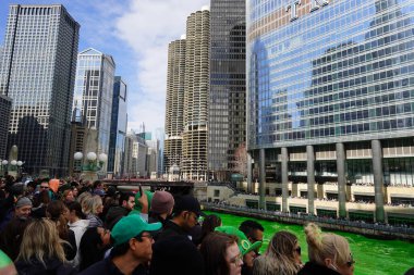 Chicago, Illinois USA - March 16th, 2024: Spectators dressed in St. Patrick colors and costumes stood and watched the Green color dyeing of the Chicago River standing in front of the Trump building clipart