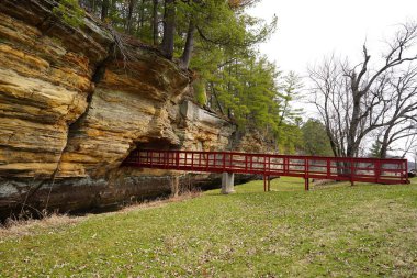 A red man-made bridge leads into a rock tunnel at Pier County Park in Rockbridge, Wisconsin a Native American historical site. clipart