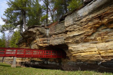 A red man-made bridge leads into a rock tunnel at Pier County Park in Rockbridge, Wisconsin a Native American historical site. clipart