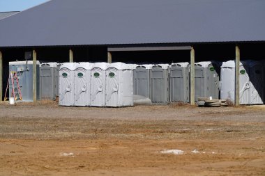 New Lisbon, Wisconsin USA - March 29th, 2024: Group of porta potties gathered together sitting outside waiting to be used. clipart