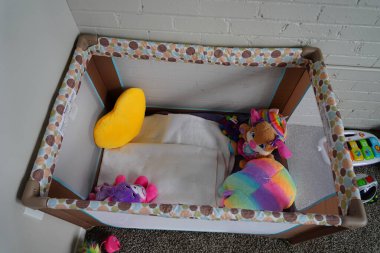 Fond du Lac, Wisconsin USA - June 20th, 2024: A brown pack 'n play with toddler girl stuffed animal toys sits in the corner of a kids bedroom. clipart