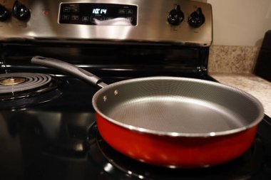 Boş bir kırmızı ve gri tava tava sobanın üstünde duruyor..