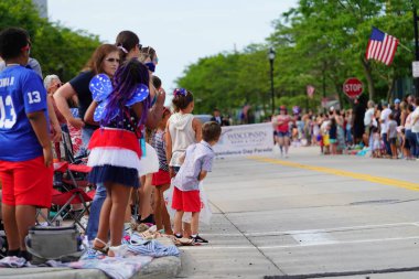 Sheboygan, Wisconsin ABD - 4 Temmuz 2024: Çocuklu aileler 4 Temmuz bayramı boyunca kaldırımlarda oturdu ve Özgürlük Festivali yürüyüşünü izledi.
