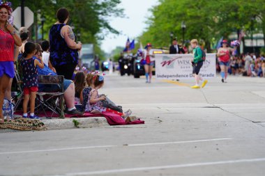 Sheboygan, Wisconsin ABD - 4 Temmuz 2024: Çocuklu aileler 4 Temmuz bayramı boyunca kaldırımlarda oturdu ve Özgürlük Festivali yürüyüşünü izledi.