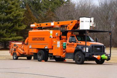 Fond du Lac, Wisconsin USA - 10 Mart 2025: Asplundh Articulated Telescopic Bucket Lift kamyonu ve odun yonga makinesi bir otoparkta kullanılmadan duruyor.
