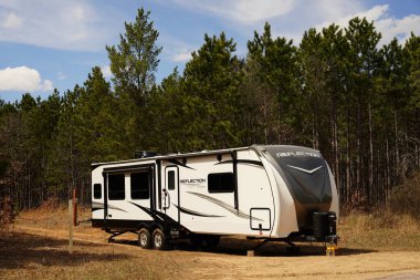Yeni Lizbon, Wisconsin ABD - 18 Nisan 2025: 5 Tekerlek Yansıma Karavanı bir ormanın yanında duruyor.