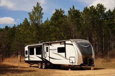 Yeni Lizbon, Wisconsin ABD - 18 Nisan 2025: 5 Tekerlek Yansıma Karavanı bir ormanın yanında duruyor.